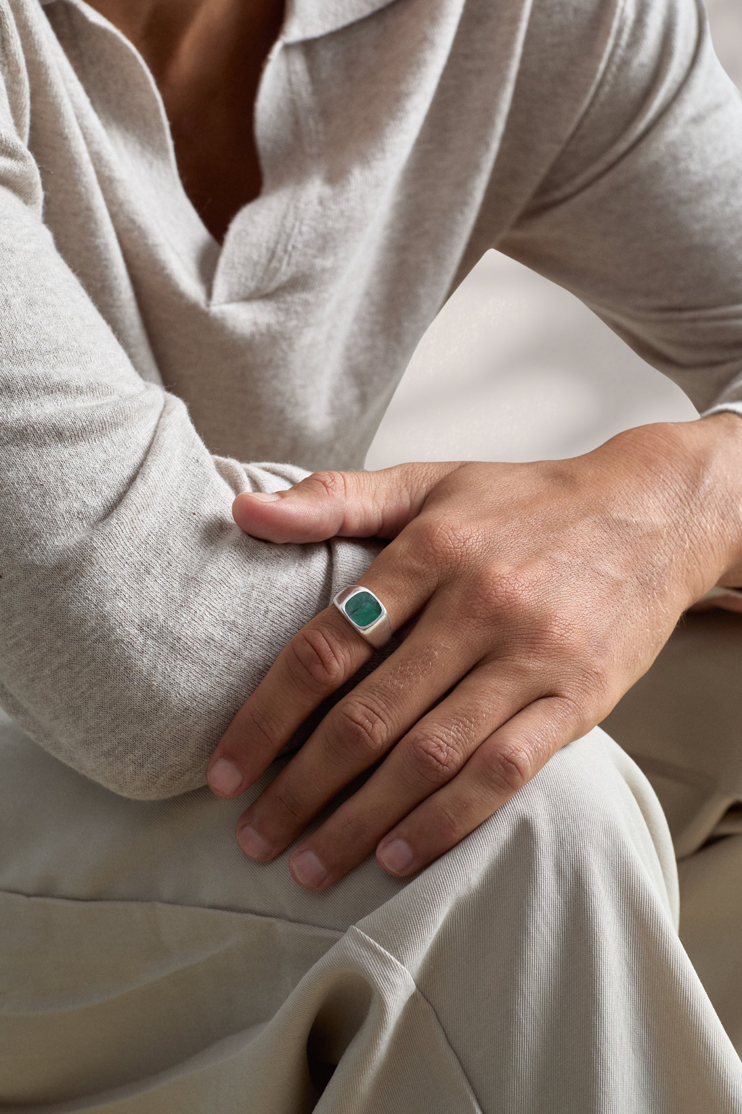 Person wearing a ring with a green gemstone on a neutral background