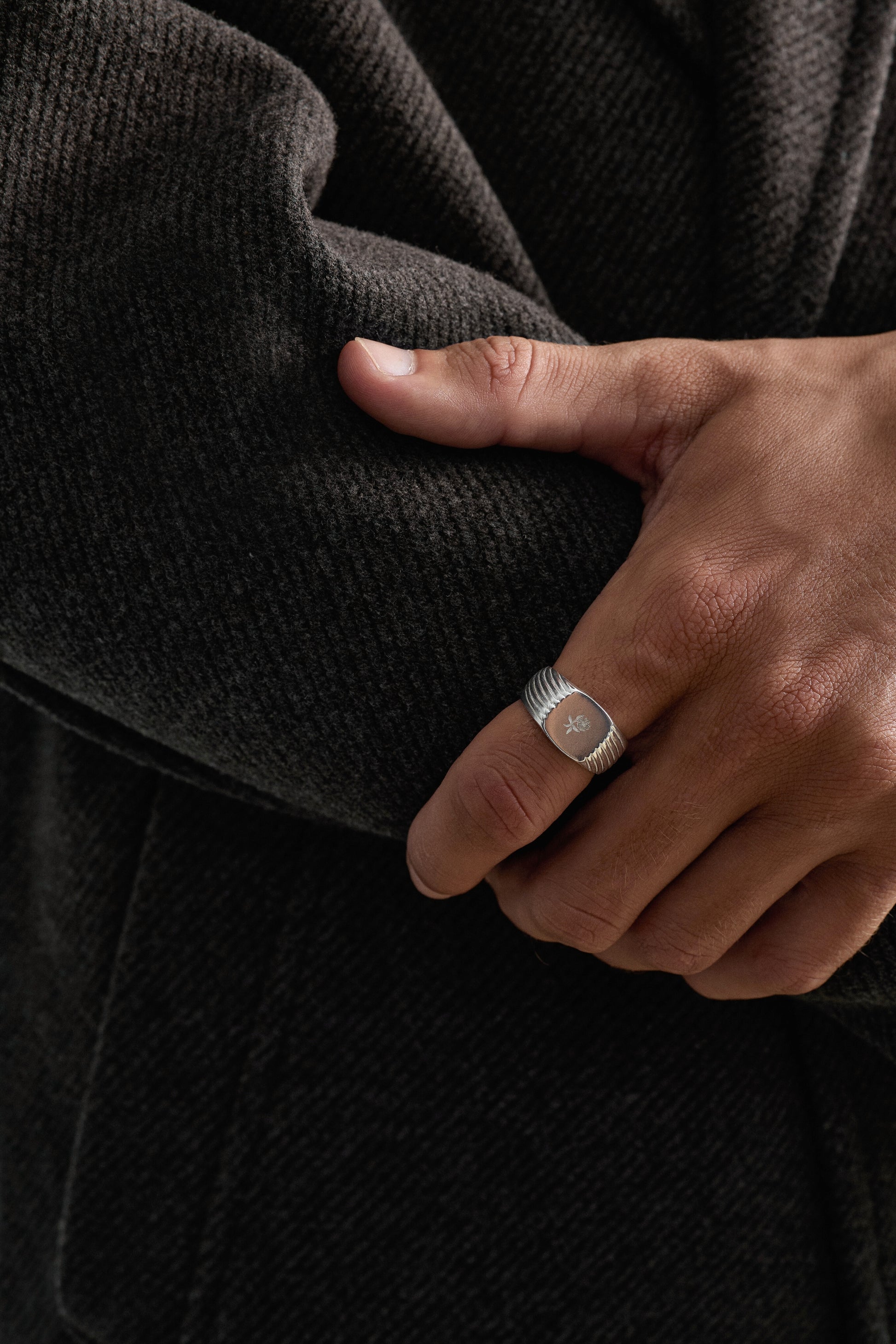 Hand wearing a silver ring on a dark background