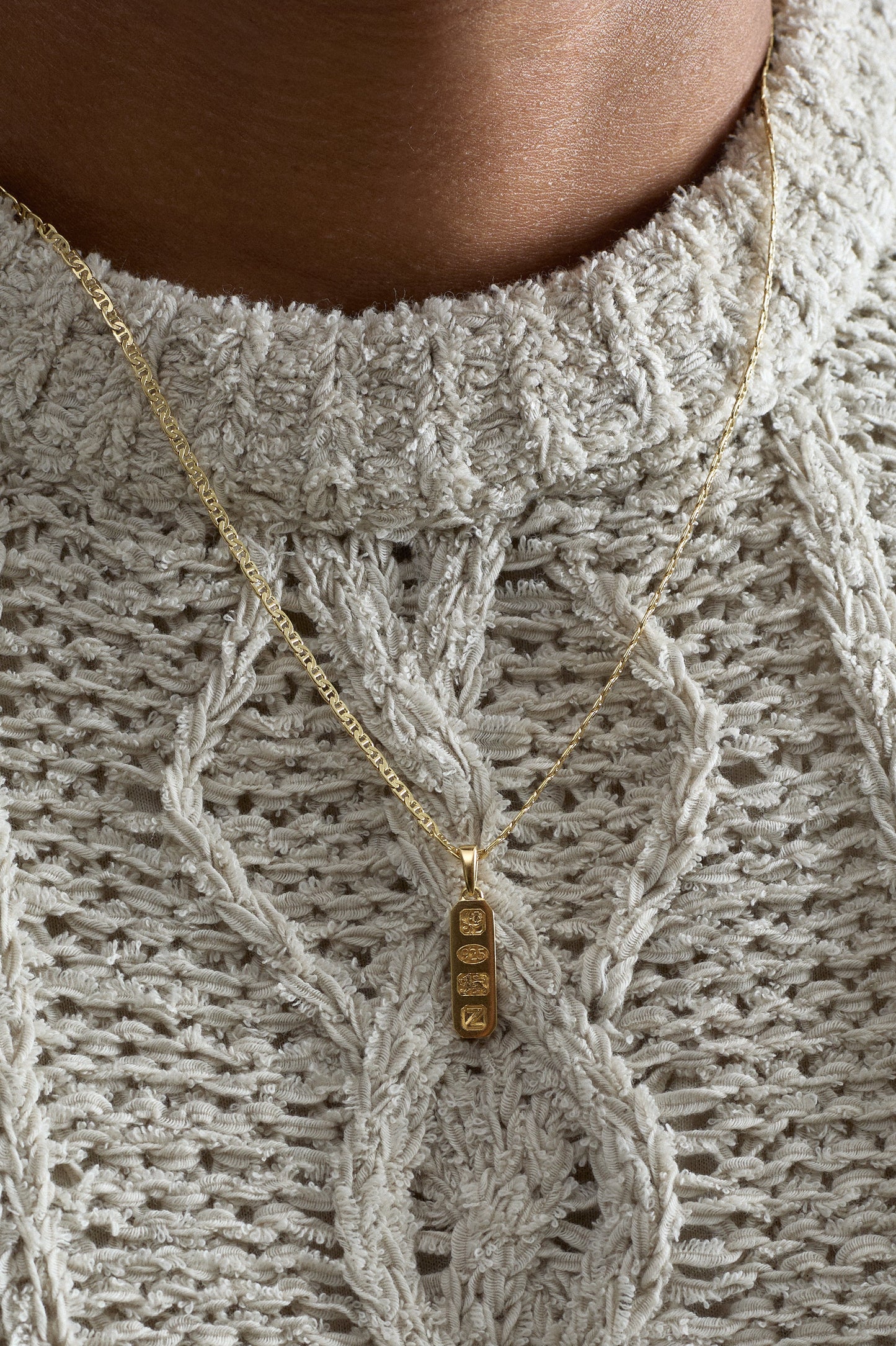 Close-up of a person wearing a textured sweater with a gold necklace featuring a gold pendant.