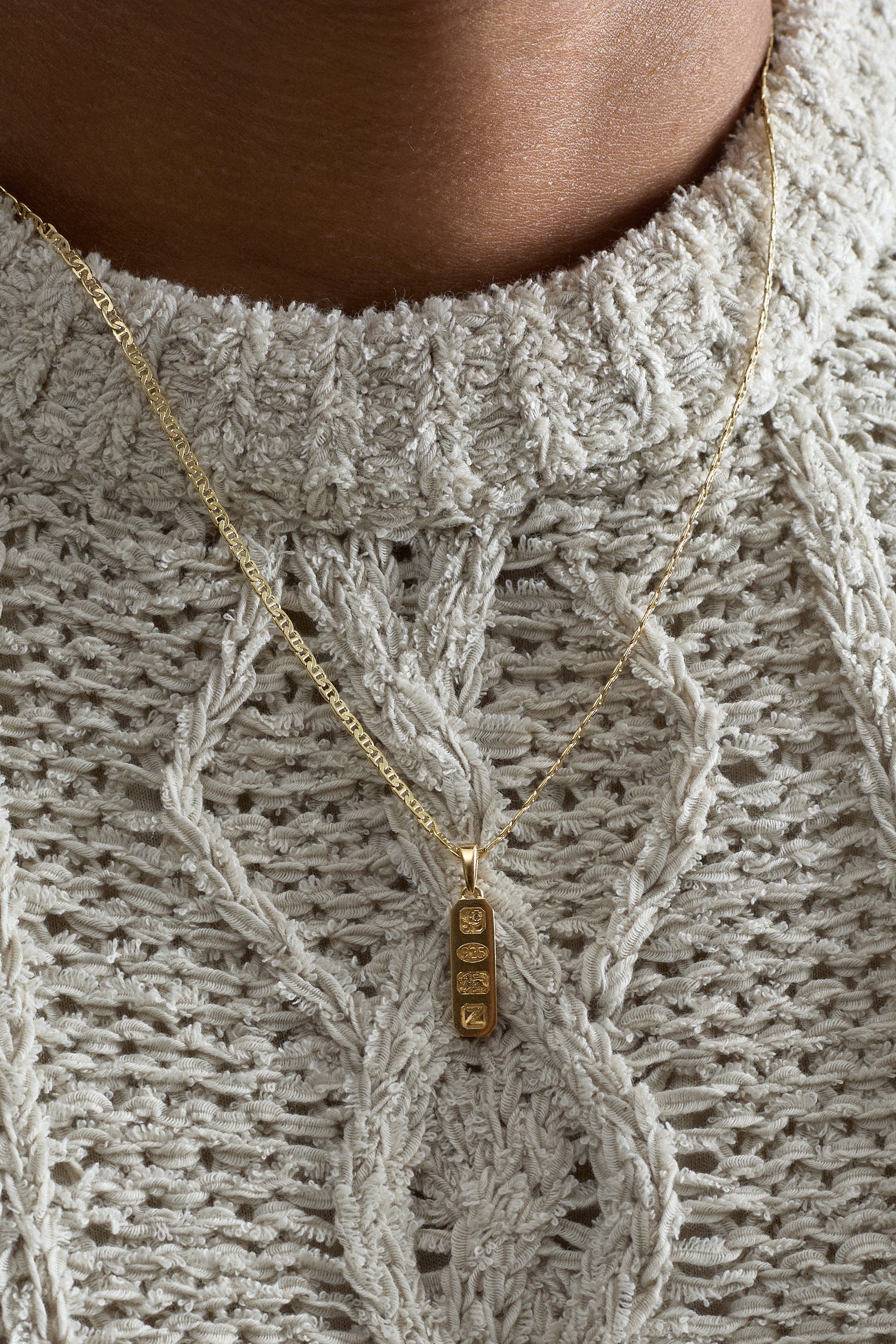 Close-up of a person wearing a textured sweater with a gold necklace featuring a gold pendant.