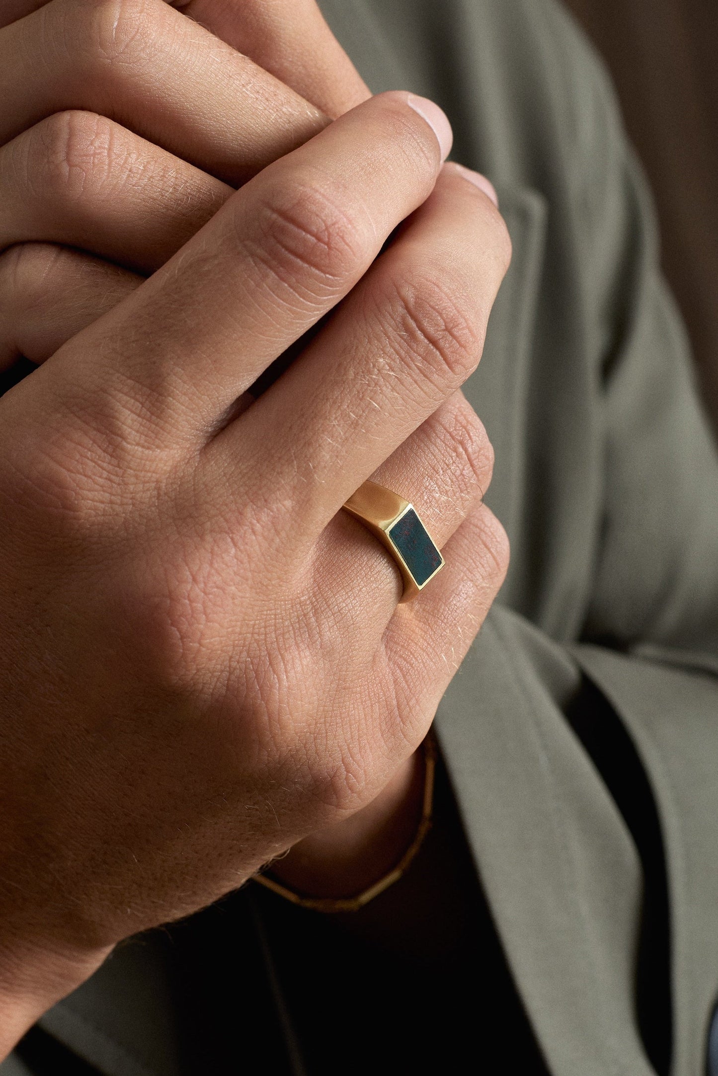 Close-up of a person wearing a ring with a green stone, clasping their hands together.